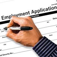 A Hand Holding A Pen Completes A Form That Is Labeled &Quot;Employment Application&Quot;