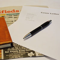 A Piece Of Paper Labeled &Quot;Cover Letter&Quot; A Pen, And A Newspaper Open To Job Advertisements.